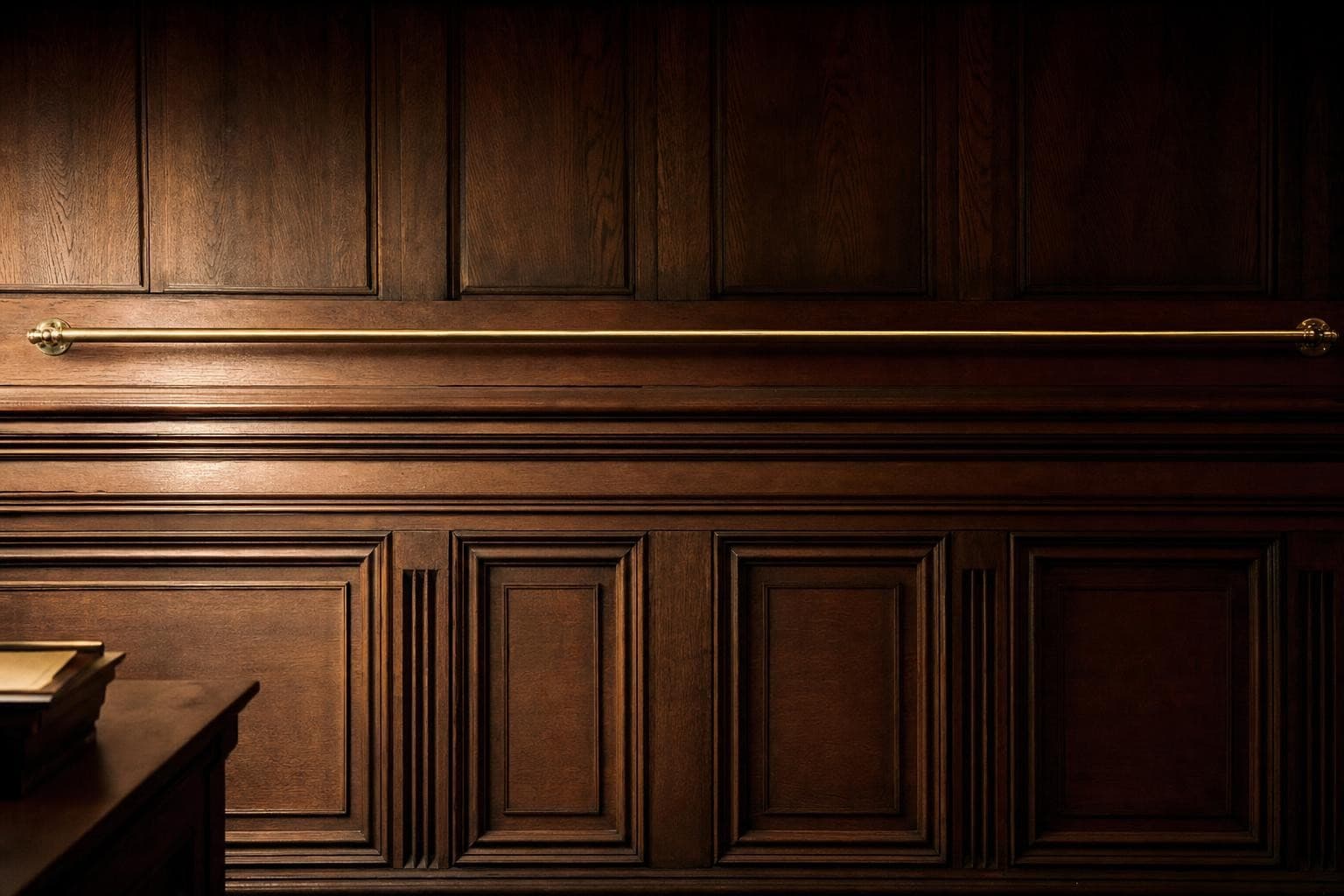 A single long horizontal polished brass rail fixed high and level across a vast wall of dark oak courtroom panelling, catching a line of warm lamplight along its length, set as one fixed threshold to be cleared.