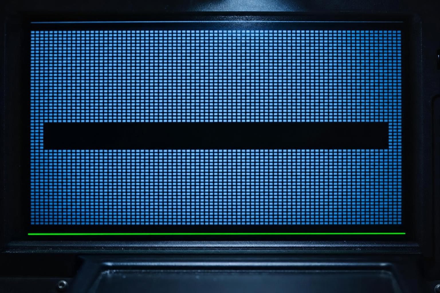 A macro of a self-lit screen in the dark showing a tight grid of glowing data blocks filling the whole readout, every cell a clean cold-blue tile, except one rectangular band in the middle that sits dead black and empty, a swath of the scan simply blank with no flag or mark around it.