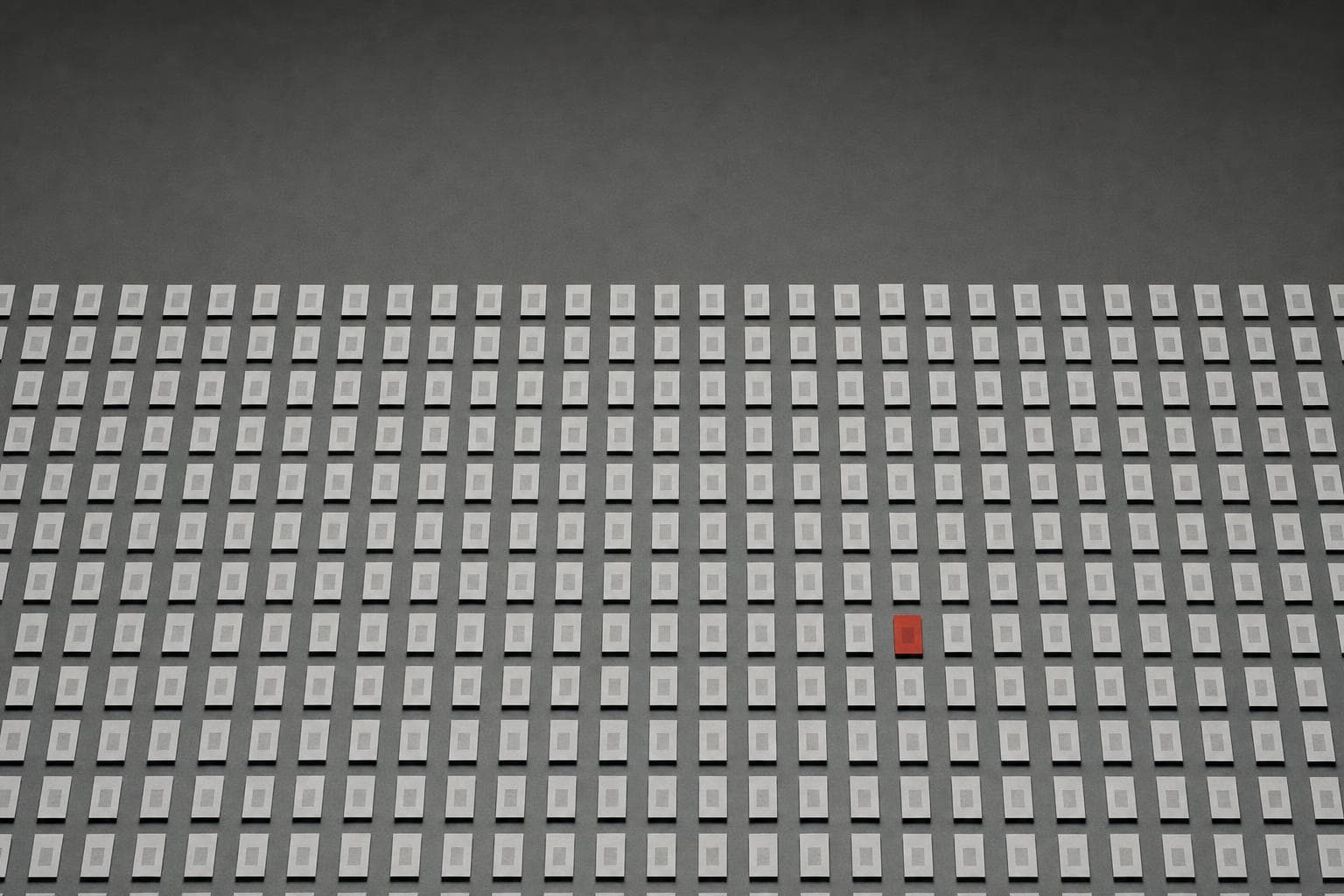 A vast grid of hundreds of near-identical grey paper comparison slips, every one matching, with a single slip glowing stark red, the lone error exposed in a sea of correct decisions.